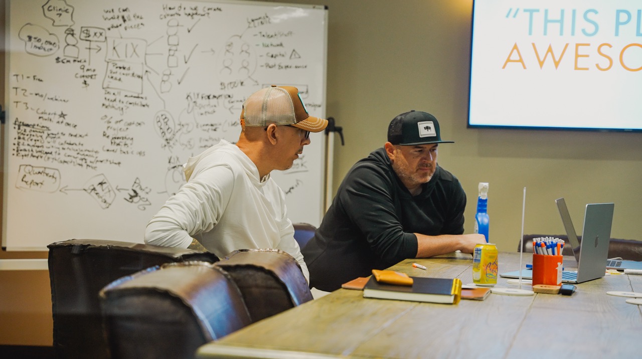 Two founders in a strategy session, whiteboard covered in plans, working out how to build a clinic.